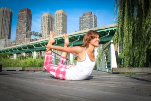 A woman practicing yoga in a park setting with a city skyline in the background.