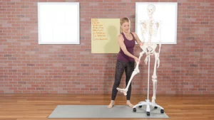A woman demonstrating hip movements in front of a skeleton.