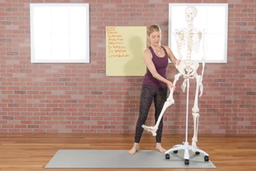 A woman demonstrating hip movements in front of a skeleton.
