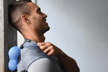Man holding a sports ball on his upper back and shoulder.