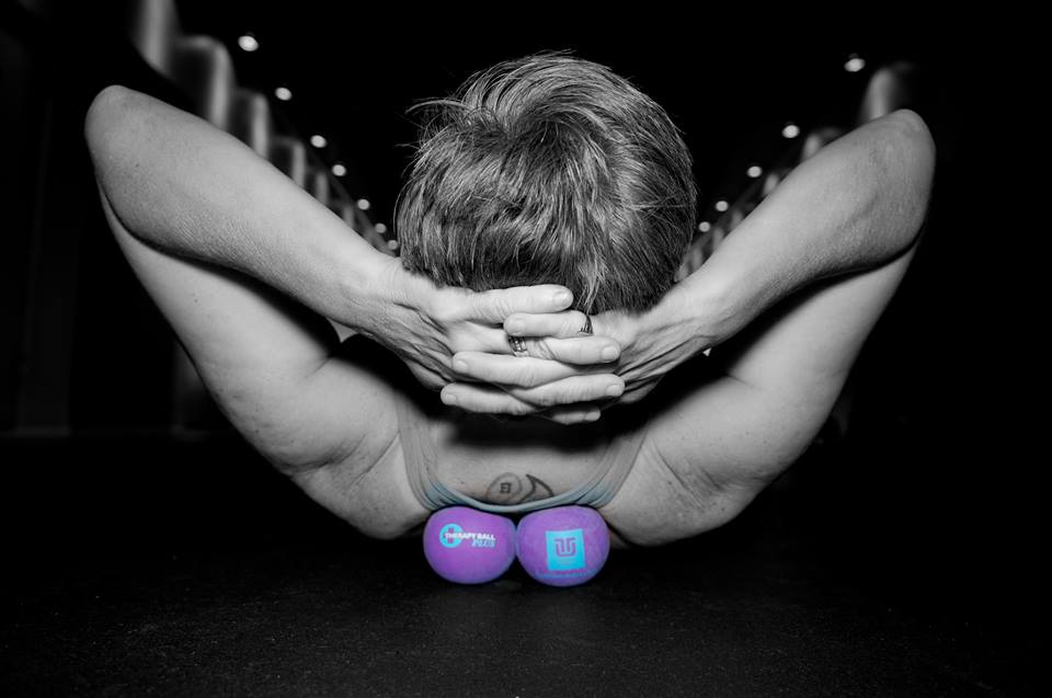 A woman holds her head with one hand while stretching over a therapy ball under her upper back.