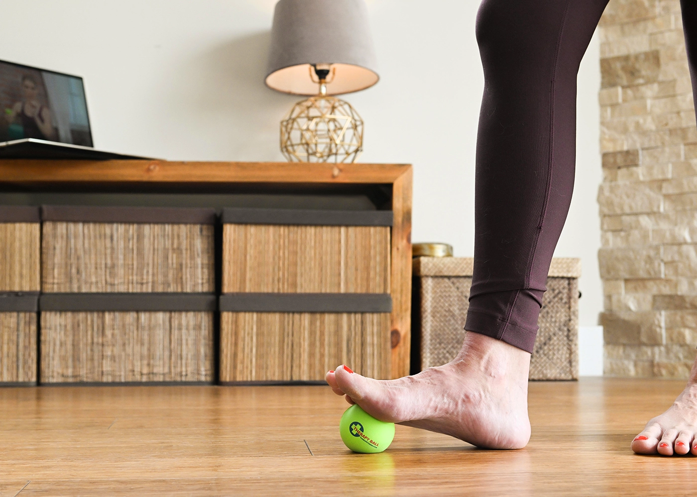 A woman poised gracefully on a wooden floor, skillfully balancing a ball on her foot.