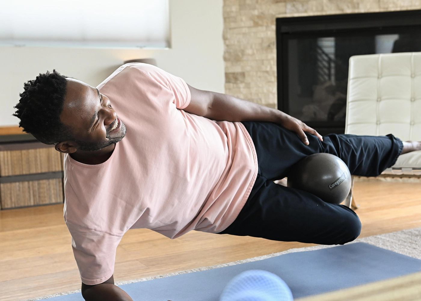 Man in side plank balancing on one leg with Coregeous ball between thighs