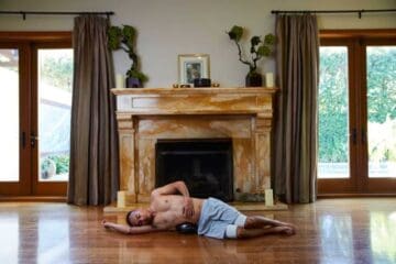 A man reclines on the floor, relaxed, in front of a warm and inviting fireplace.