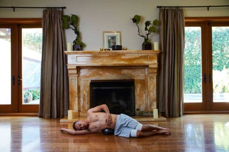 A man reclines on the floor, relaxed, in front of a warm and inviting fireplace.