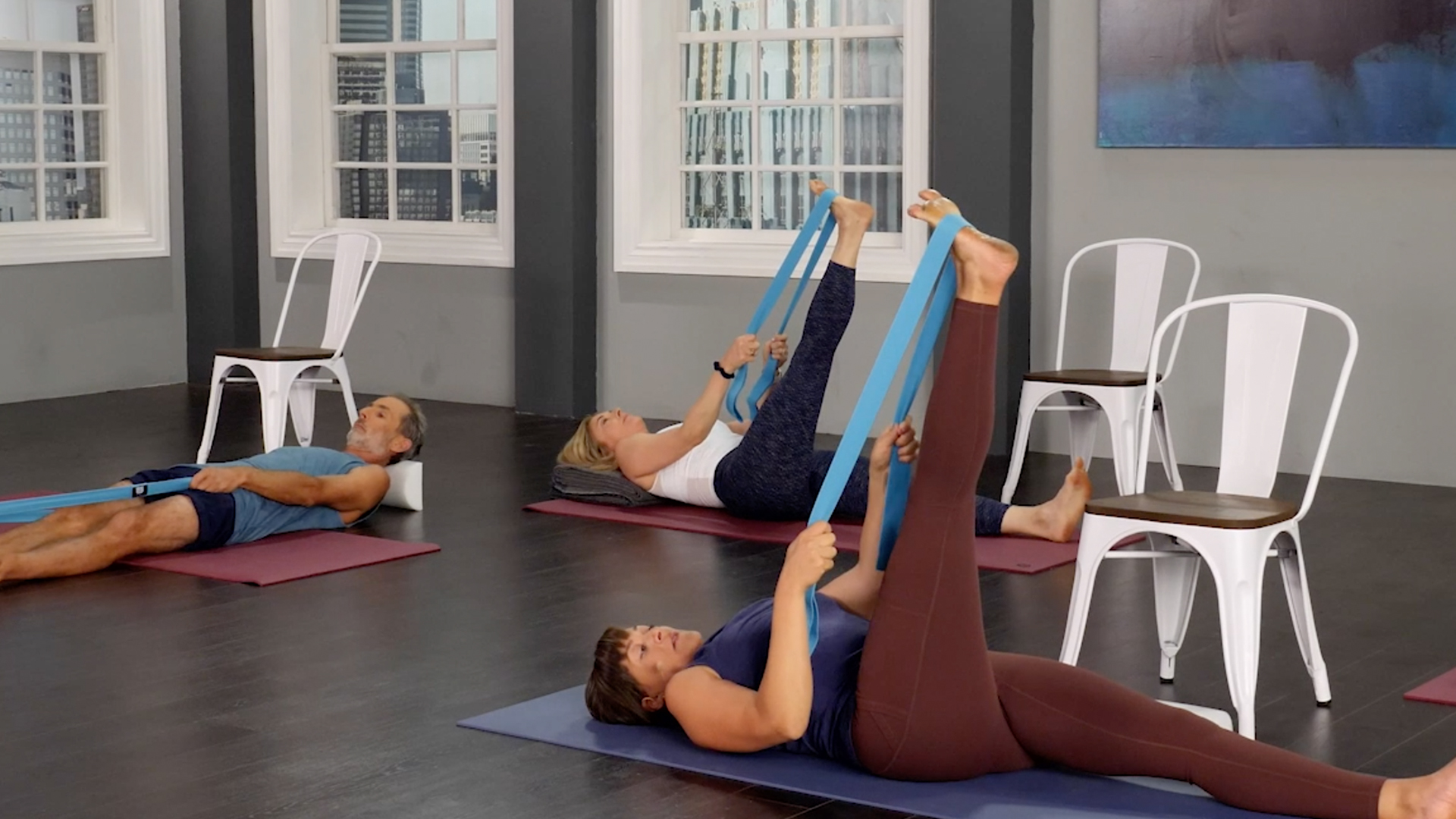 People perform leg stretches, lifting one leg with the help of ropes.