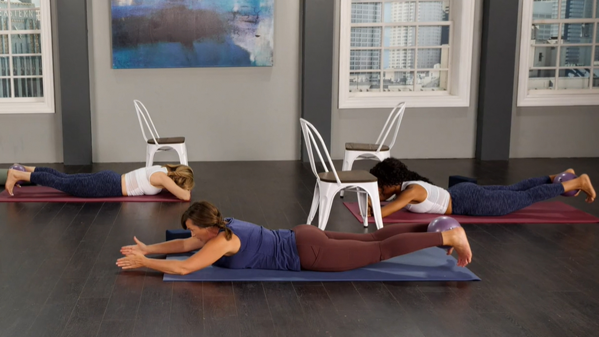 A group of women exercises on yoga mats with yoga balls between their legs.