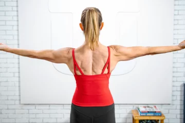 A woman in a red tank top performs a back exercise, focusing on her posture and strength training technique.