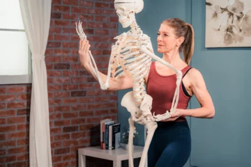 A woman is standing in front of a large, anatomical skeleton.