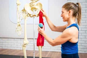 A woman stands holding a ball in one hand and a skeleton in the other.