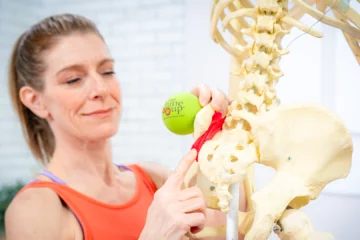 A woman is using a ball to apply pressure to the hip area of a skeleton.