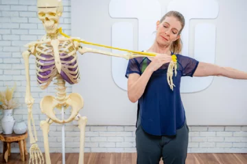 A woman performing a shoulder stretch with a resistance band and a skeleton model.