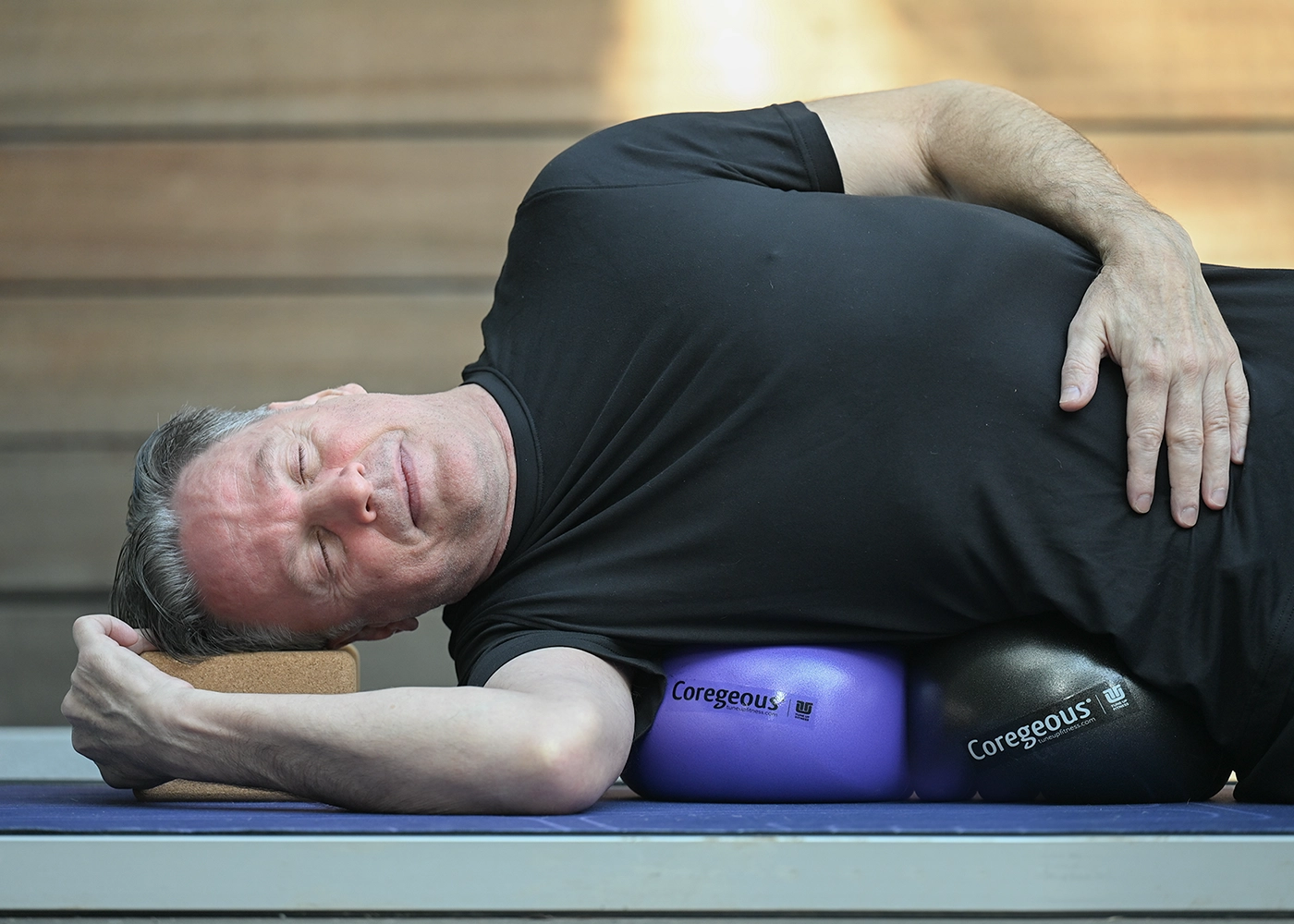 New_to_TUF_Expand_Emotional_Reslience_Image_This-one (1) Person lying sideways on a mat with a cork block supporting the head and two Coregeous balls under the torso, eyes closed, demonstrating a guided fascia release and mobility exercise in a calm studio environment, promoting mindful tension relief and emotional resilience.