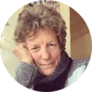 Gay Leechman A black-and-white portrait of a woman with short curly hair, wearing a textured sweater and scarf, resting her chin on her hand and gazing thoughtfully at the camera.