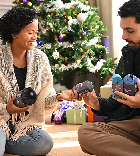 Hero_Carousel_Second Set_Right Two people exchanging Tune Up Fitness massage balls while sitting by a Christmas tree, sharing a moment of wellness and recovery at home.